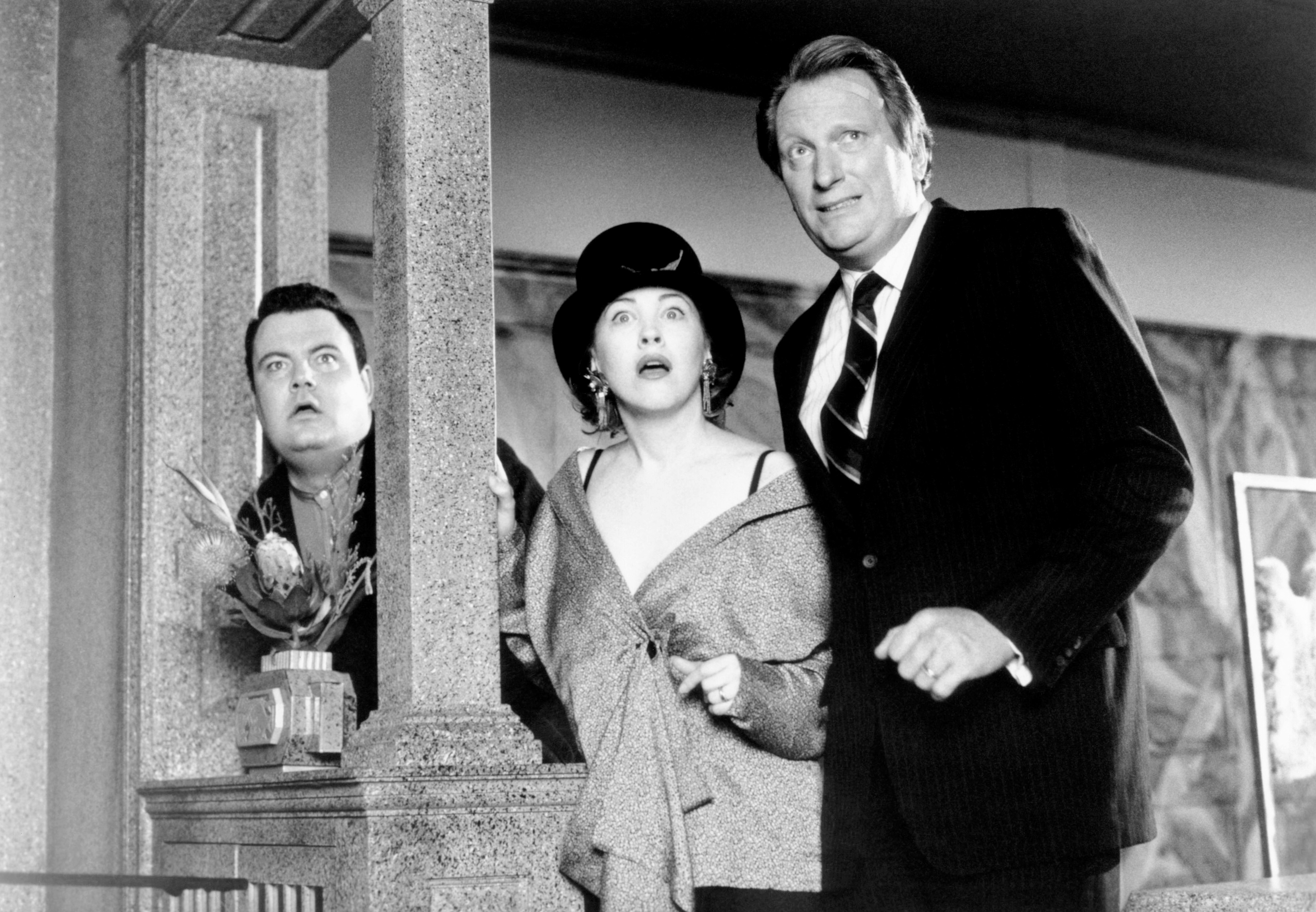 En scene fra en klassisk film som viser tre personer i dramatiske, tidstypiske klær, som virker overrasket eller skremt