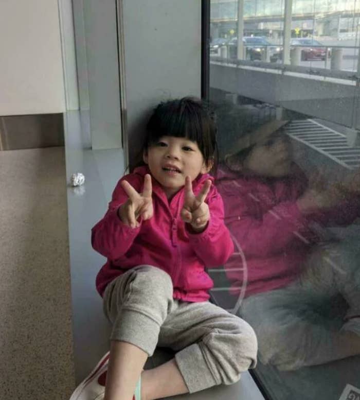 Child sitting by a model   indoors, smiling and making bid    signs with some  hands