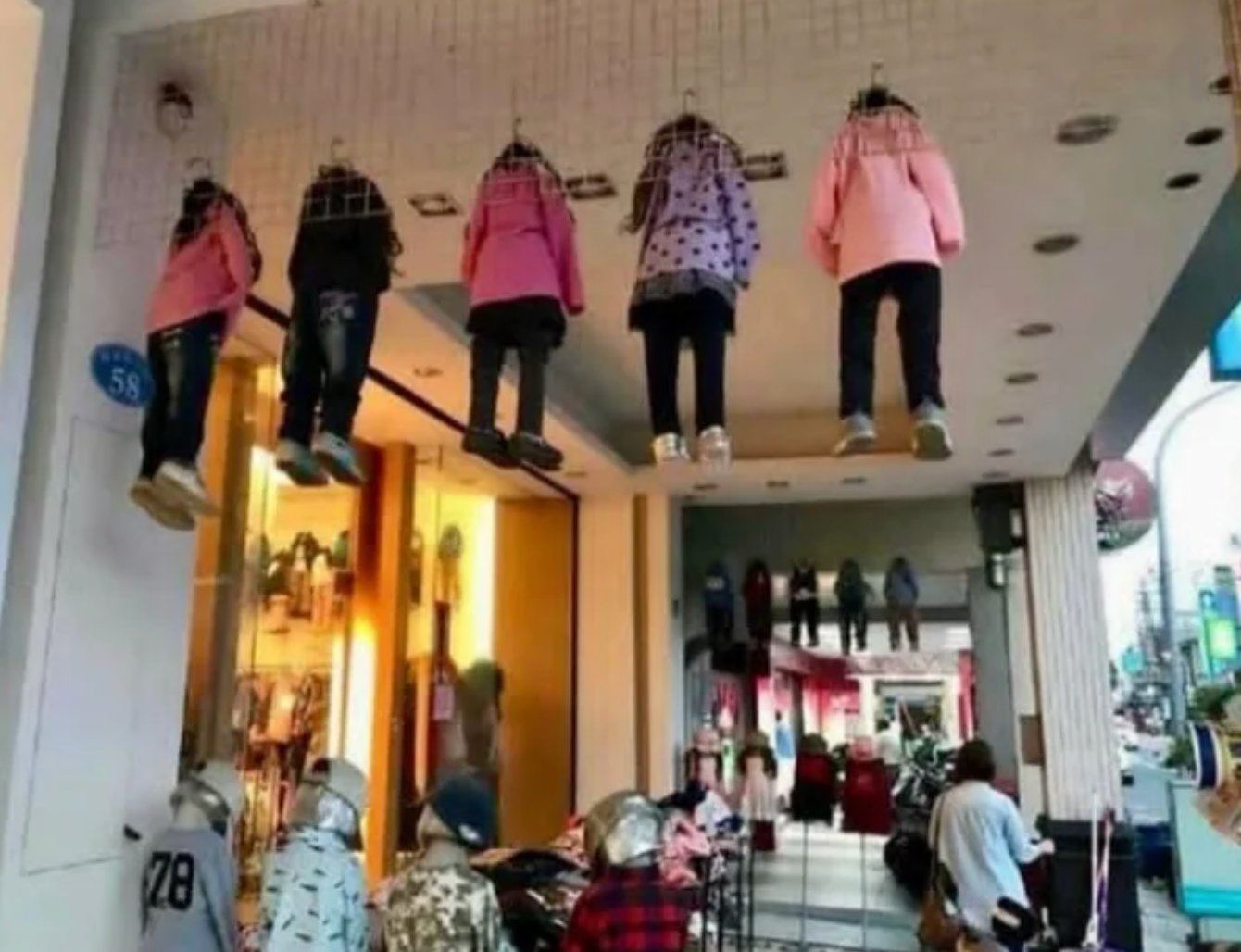 Mannequins dressed successful casual clothing, including hoodies and jeans, bent from the ceiling successful a store's outdoor display. Passersby are disposable below
