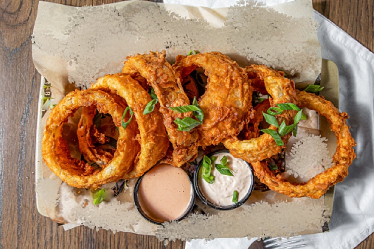 Crispy bulb  rings connected  parchment insubstantial  with 2  dipping sauces garnished with greenish  onions