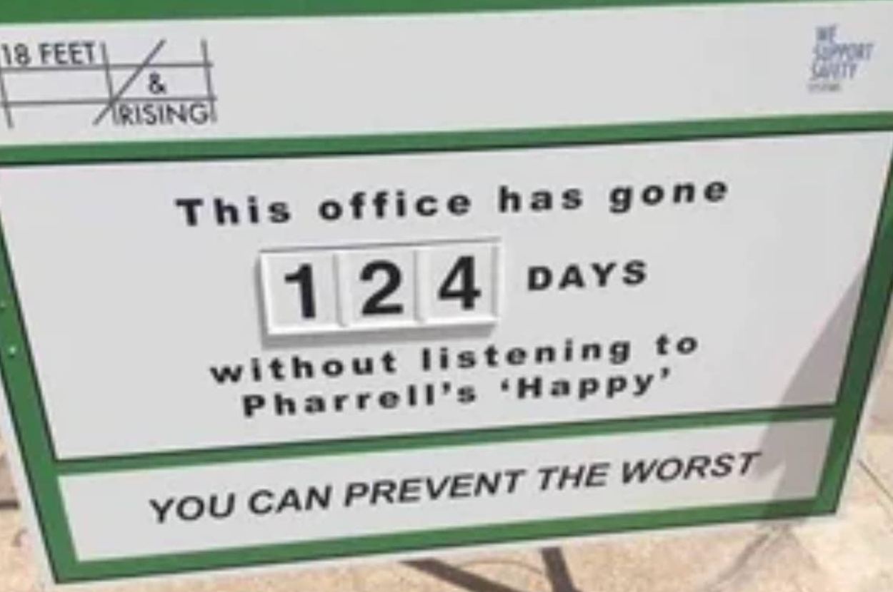 Sign reads: "This office has gone 124 days without listening to Pharrell's 'Happy.'" Encourages maintaining this streak for safety
