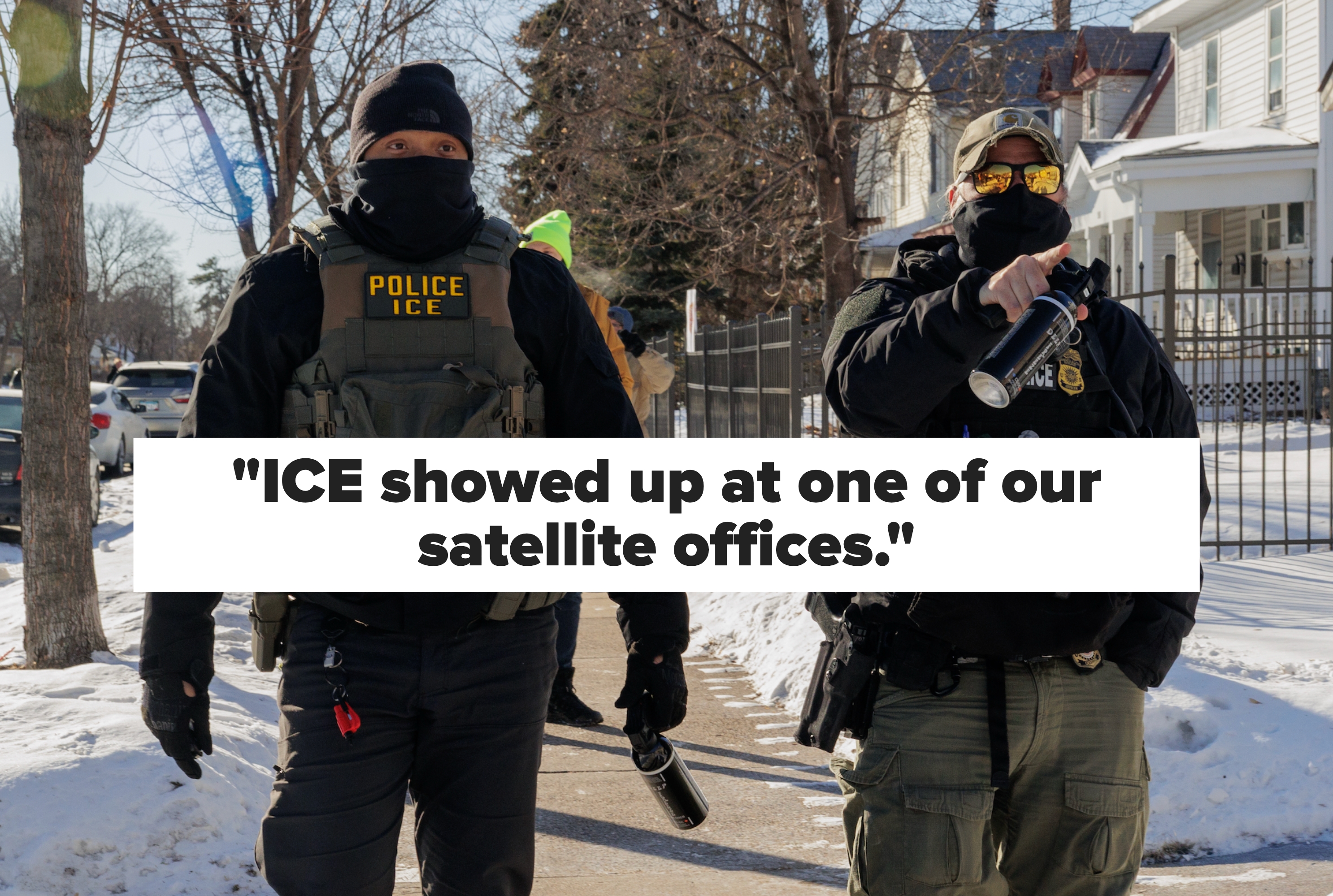 To ICE-offiserer iført taktisk utstyr og ansiktsdekker går på en snødekt gate og holder vannflasker. Hus og et gjerde langs bakgrunnen