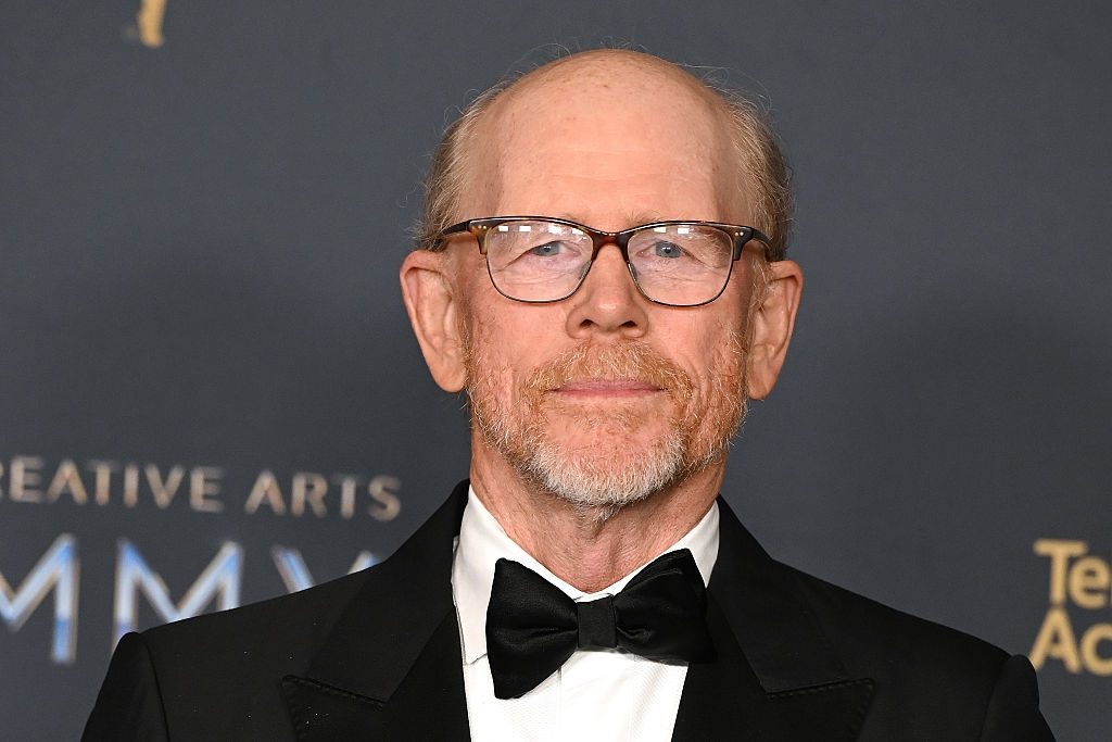 A antheral   successful  a tuxedo with a bow necktie  stands astatine  an lawsuit   backdrop. He has glasses and a beard