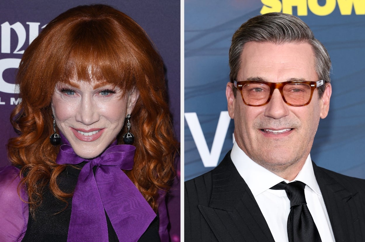 Two people at a media event. Left: Woman with wavy hair, wearing a bow-tied top. Right: Man with glasses, in a suit and tie. Both smiling at the camera