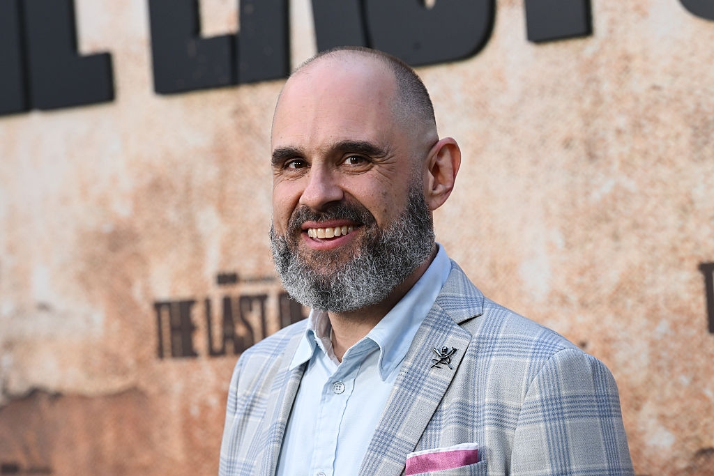 Person successful  a plaid suit   connected  a reddish  carpet, smiling astatine  an lawsuit   for "The Last of Us."