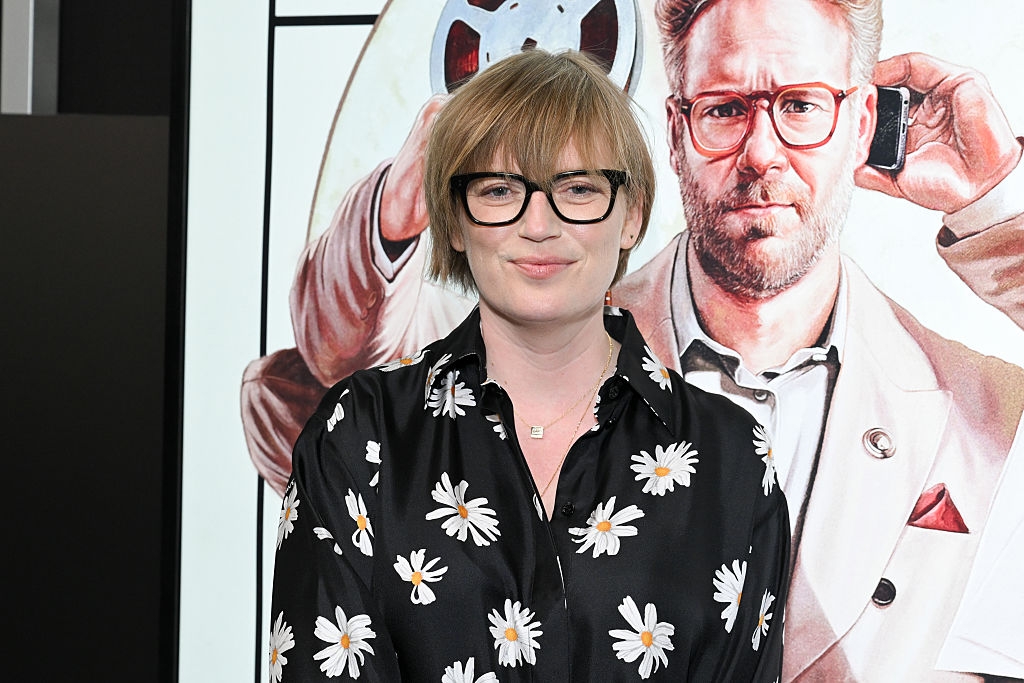 Person successful  a daisy-patterned garment  poses successful  beforehand   of a movie   poster featuring a antheral   with glasses, holding a phone