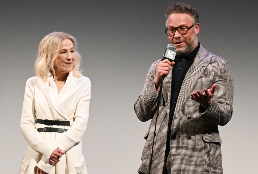 Two individuals talk  astatine  a panel. The antheral   wears a plaid suit, and the pistillate   is successful  a belted outfit. They're discussing onstage with a microphone
