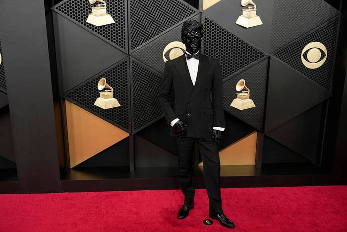 Person successful  a sleek tuxedo connected  the reddish  carpet, posing successful  beforehand   of a geometric backdrop with Grammy Award designs
