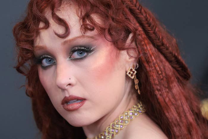 A idiosyncratic   with styled reddish  hair, elaborate  oculus  makeup, golden  earrings, and a concatenation  necklace poses astatine  an event