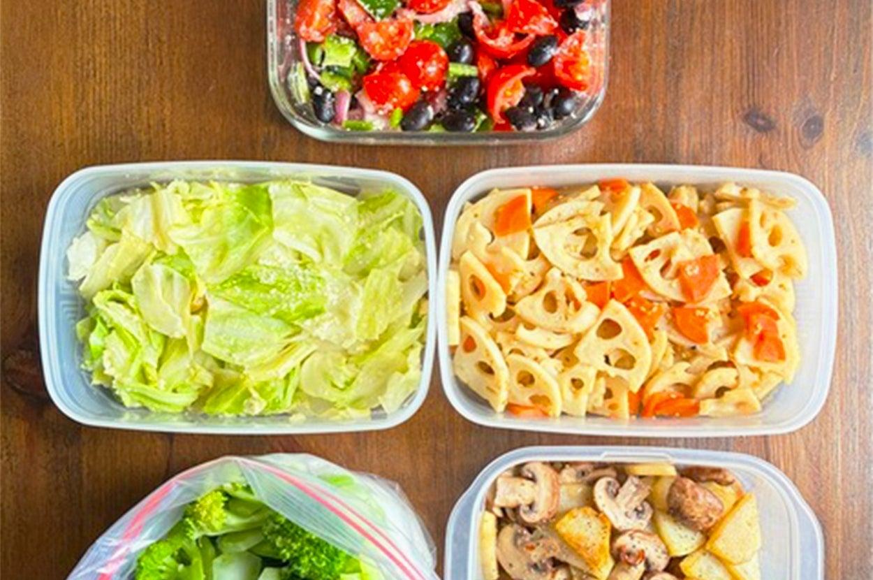 プラスチック容器に入ったサラダや野菜の準備済み食材がテーブルに並んでいます。