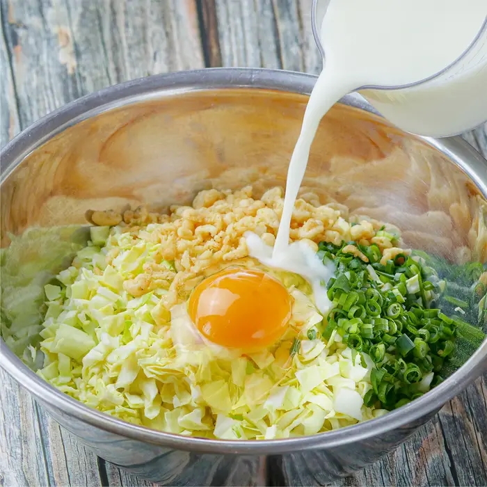 大きなボウルにキャベツ、卵、刻んだねぎが入って、牛乳が注がれている。