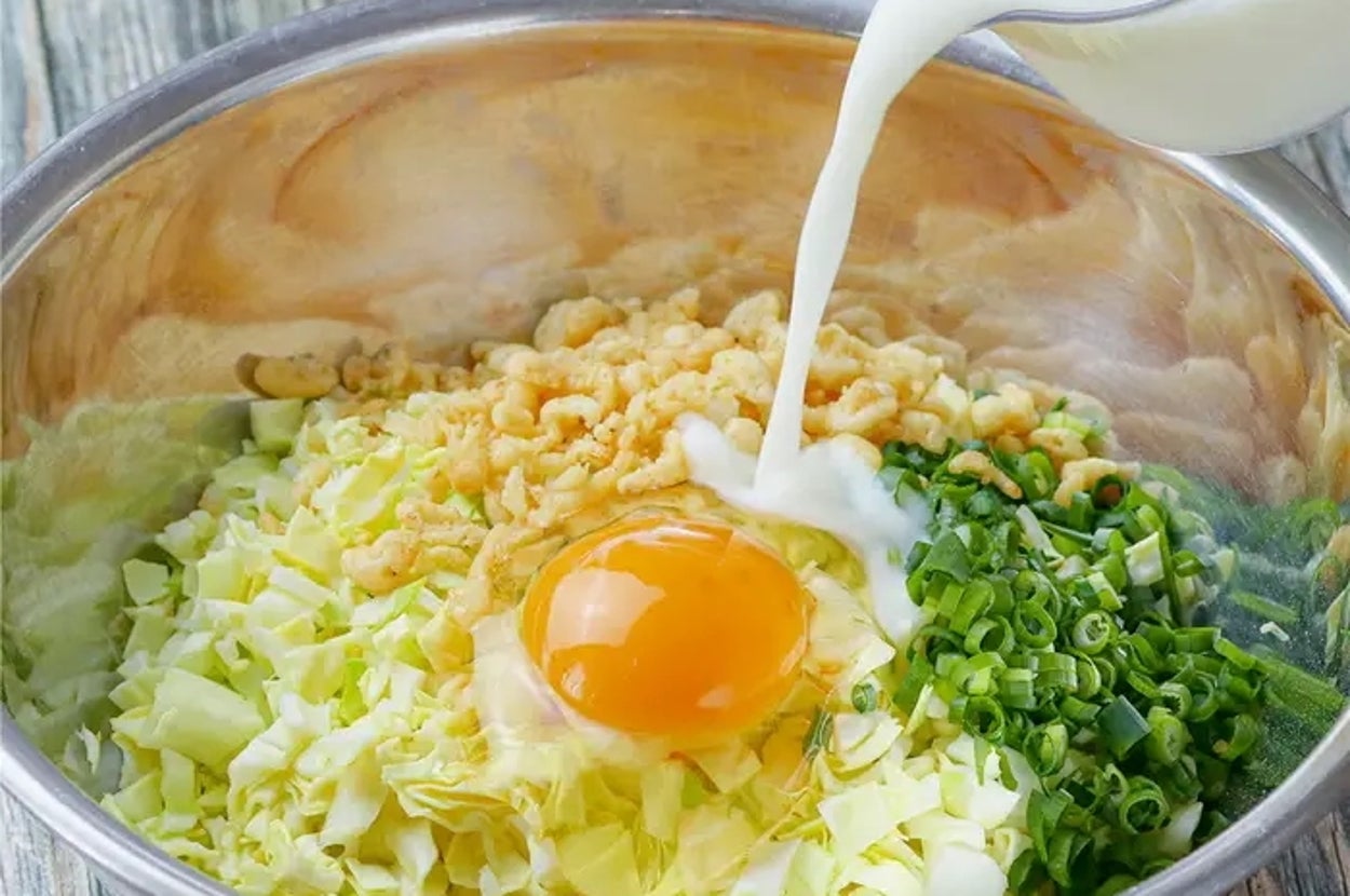 大きなボウルにキャベツ、卵、刻んだねぎが入って、牛乳が注がれている。