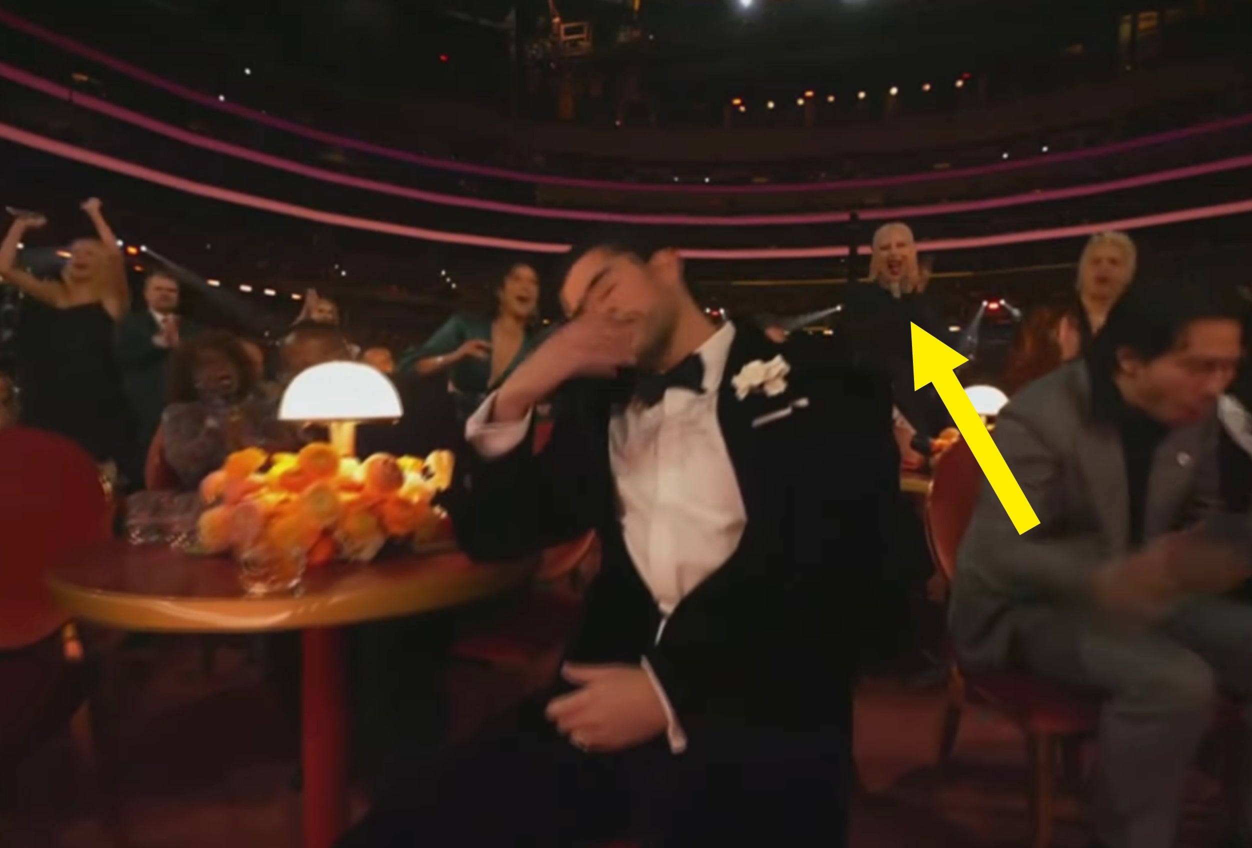 A idiosyncratic   successful  a tuxedo is seated and dabbing with a joyful assemblage  astir   them successful  a theatre  setting