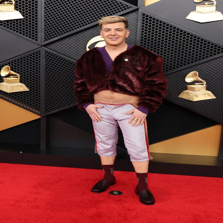 Person on red carpet wearing a plush cropped jacket, fitted capri pants, and loafers, with Grammys decor in the background