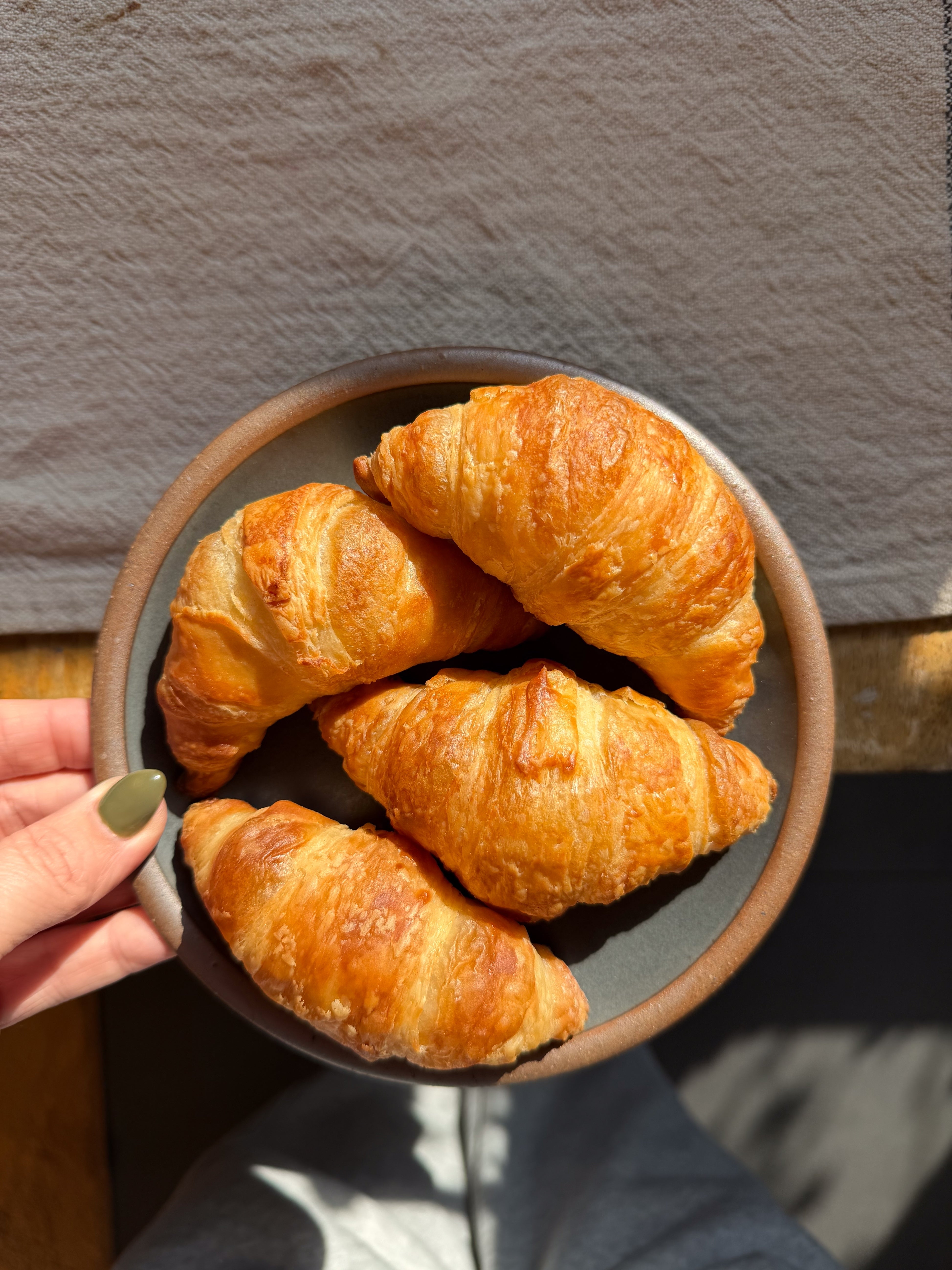 Four croissants on a round plate held by a person with a manicured hand
