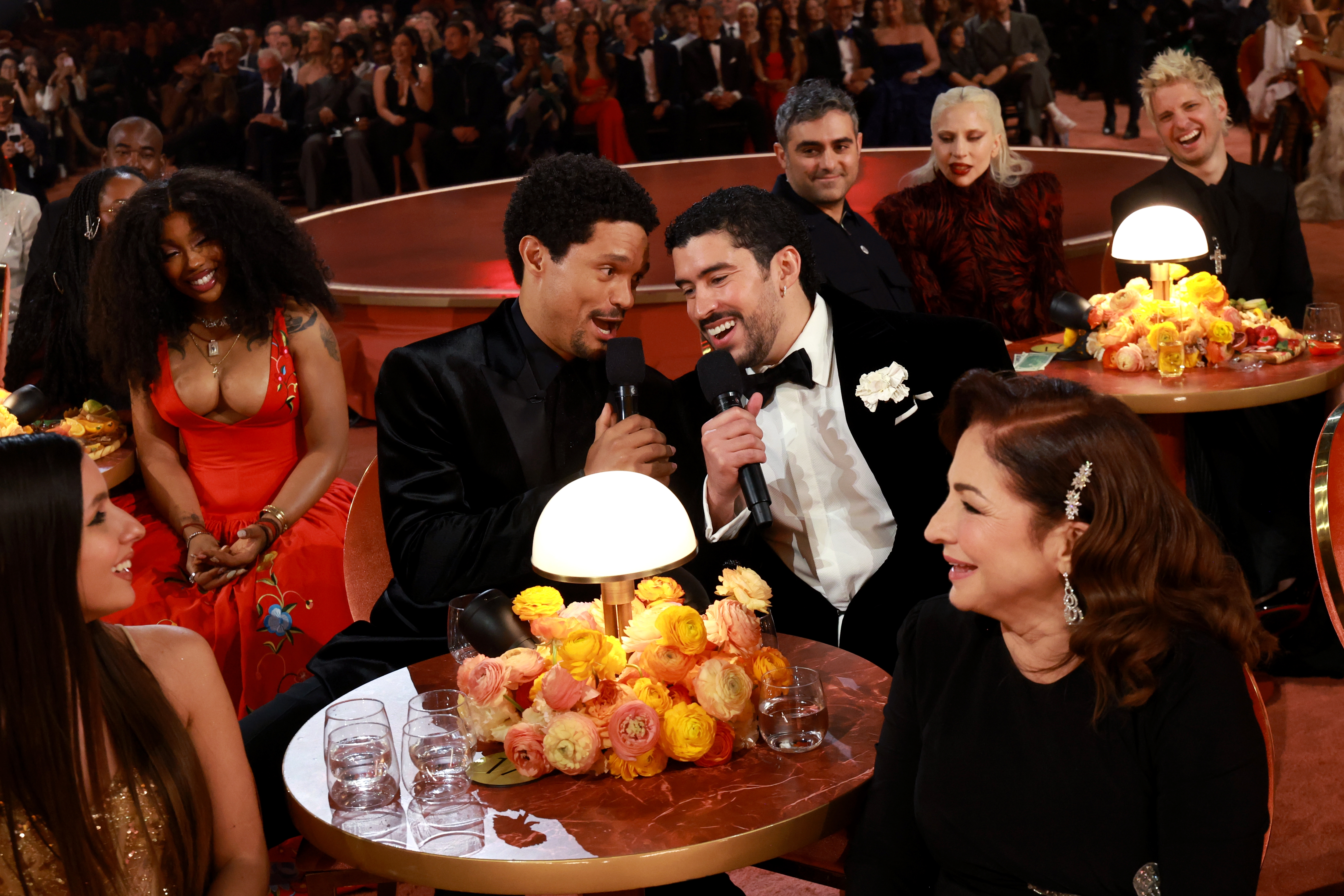 Group of radical   astatine  a ceremonial  event, 2  men singing into 1  microphone, others astir   them smiling and engaged