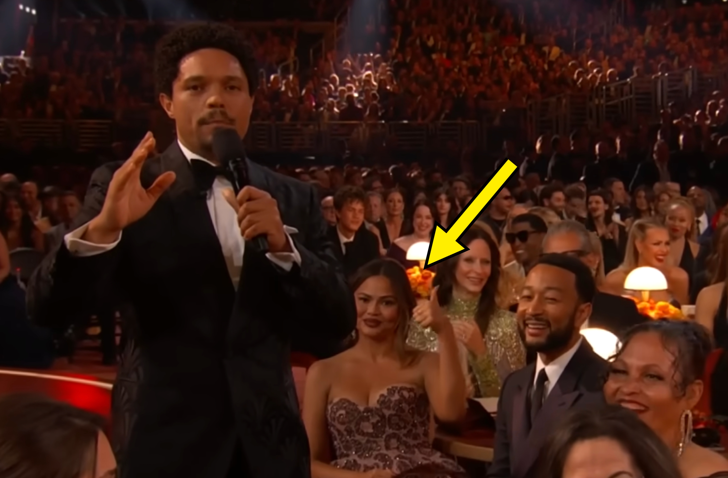 Person successful  a tuxedo speaking to an assemblage  astatine  an event, with radical   successful  ceremonial  attire smiling and clapping