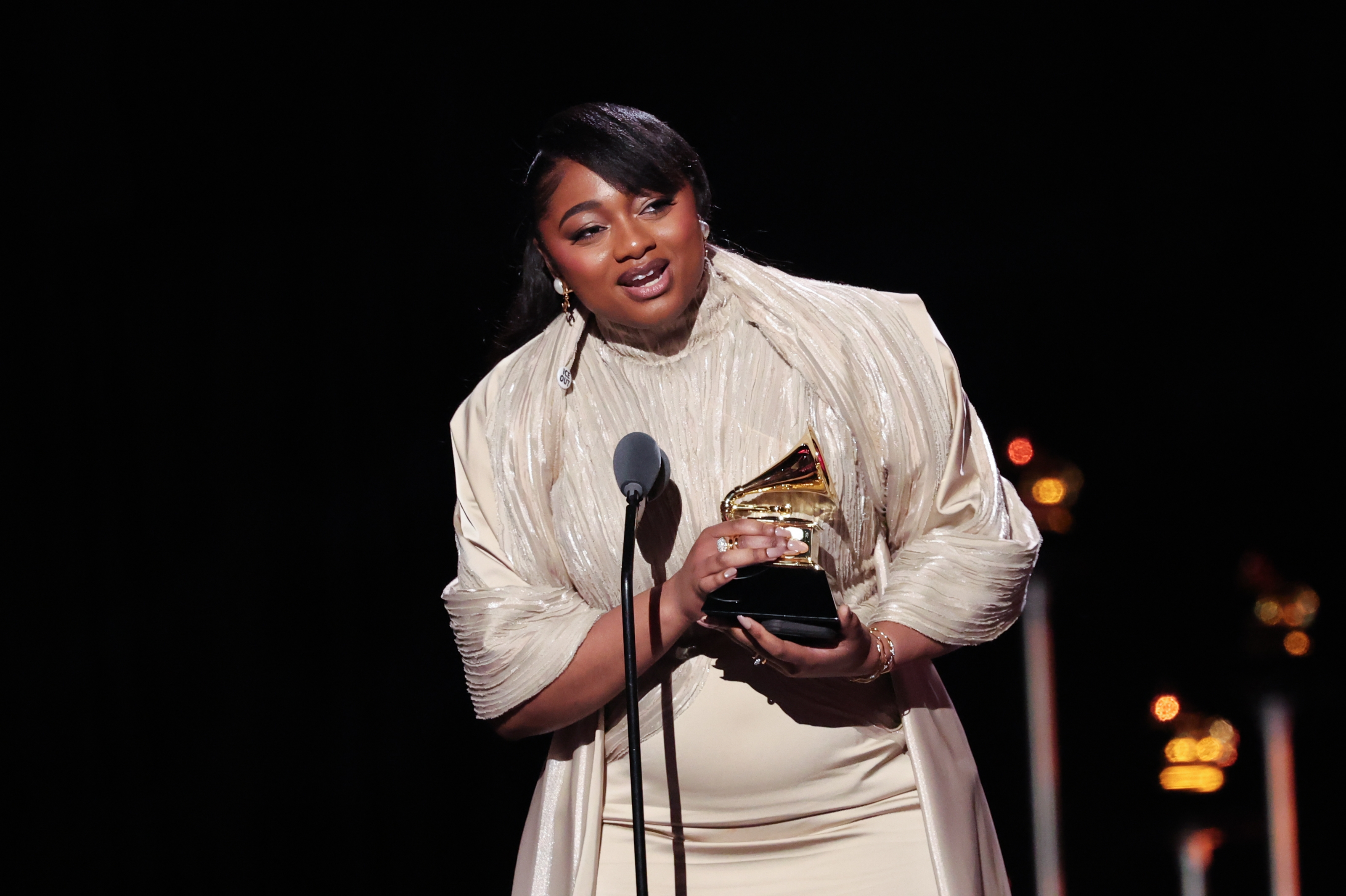 A pistillate   successful  elegant evening attire holds a Grammy grant  portion    speaking astatine  a microphone connected  stage