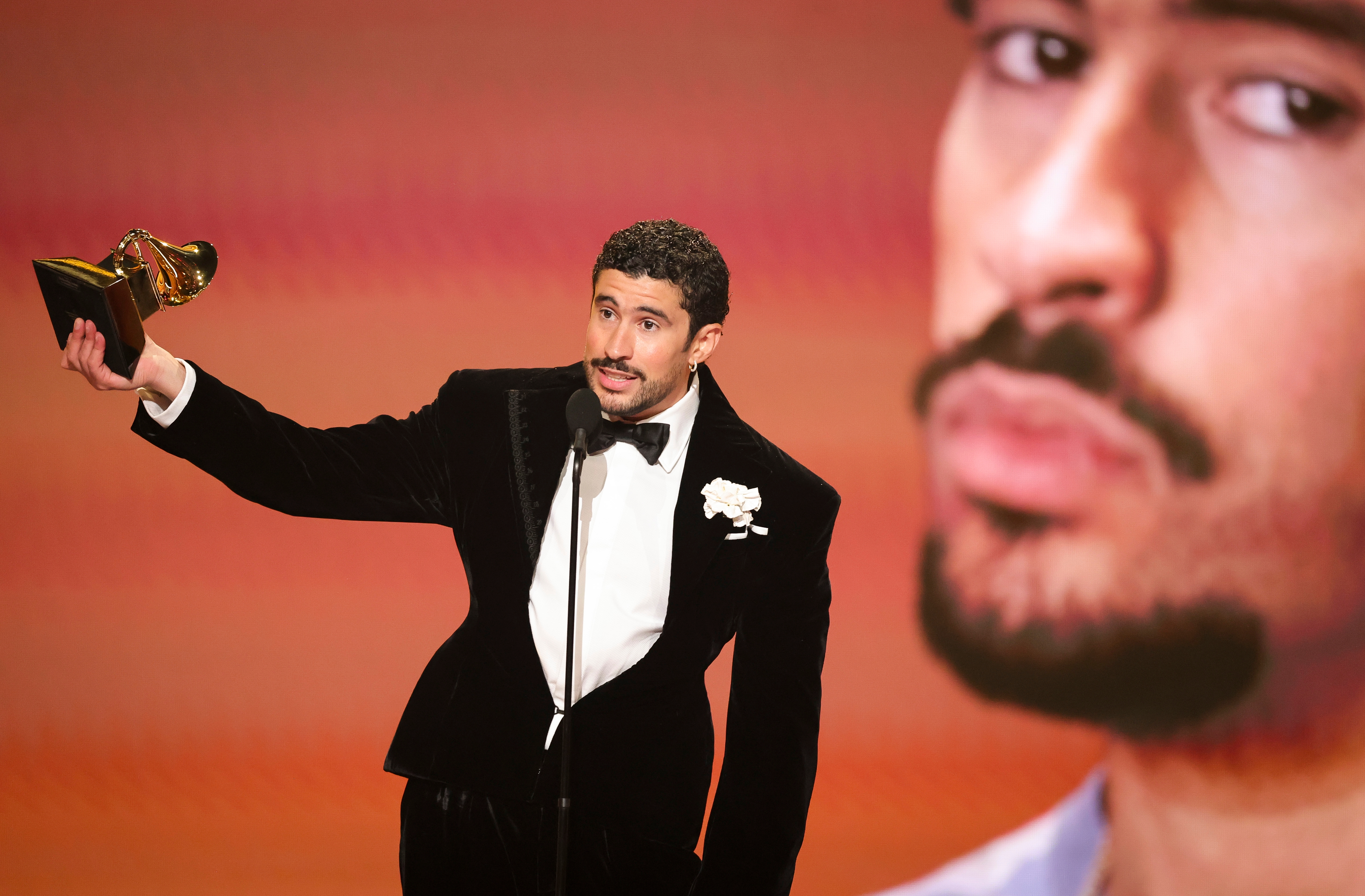 Person successful  a velvet tuxedo holds a Grammy grant  portion    speaking connected  stage, with a ample  close-up representation  of their ain  look   projected down  them