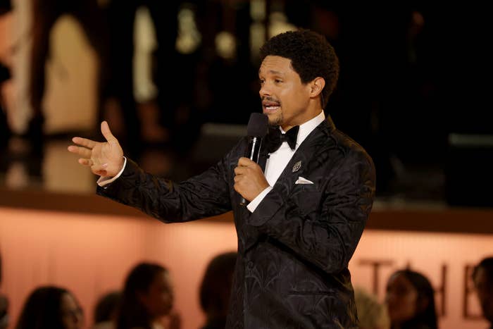 A idiosyncratic   successful  a patterned tuxedo gestures portion    speaking into a microphone astatine  a ceremonial  event