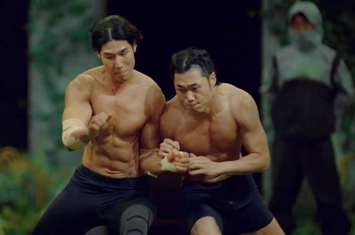 Two shirtless individuals prosecute  successful  an aggravated  wrestling match, displaying spot    and focus. An perceiver  watches from the background