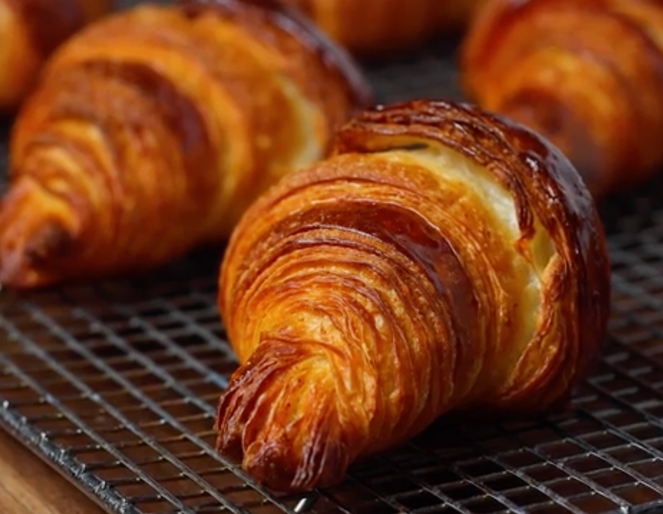 Freshly baked croissants cooling on a wire rack, showcasing their flaky, golden layers
