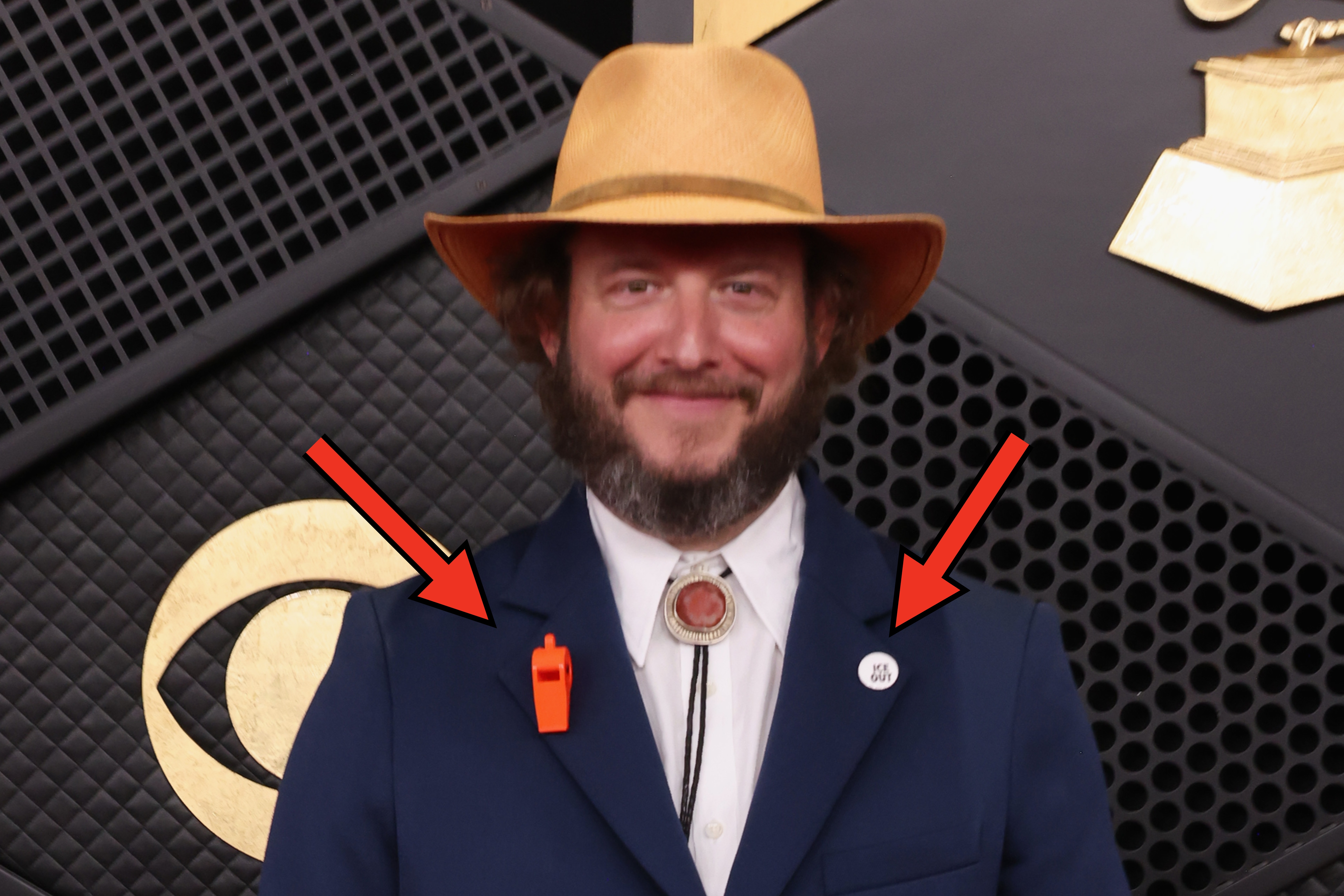 A idiosyncratic   connected  a reddish  carpet successful  a bluish  suit, bolo tie, and wide-brimmed hat, lasting  successful  beforehand   of Grammy Award-themed decor