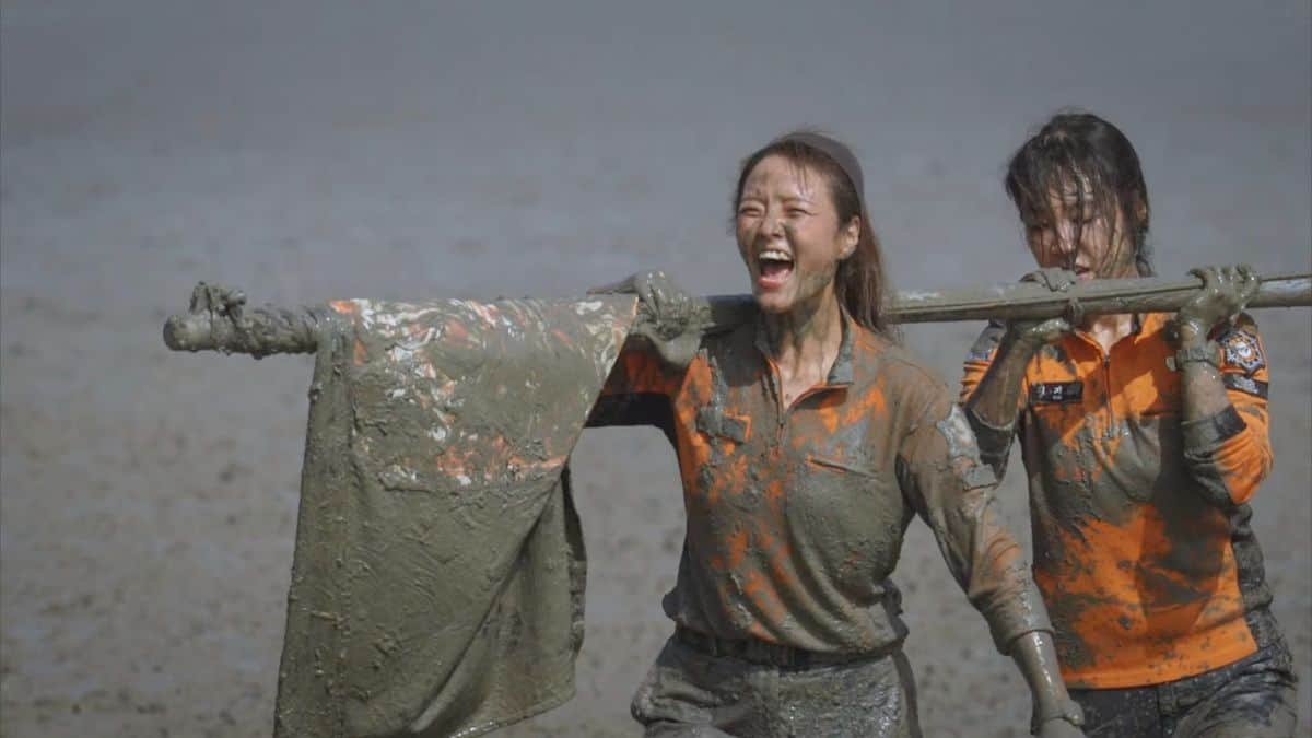 Two radical   covered successful  mud, smiling and walking, carrying a ample  cloth connected  a stick, suggesting playful outdoor amusive  oregon  a mud event