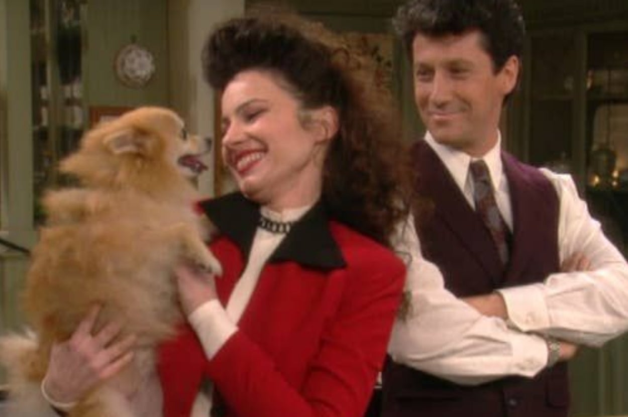 A woman joyfully holds a small fluffy dog, while a man in a vest watches with a smile