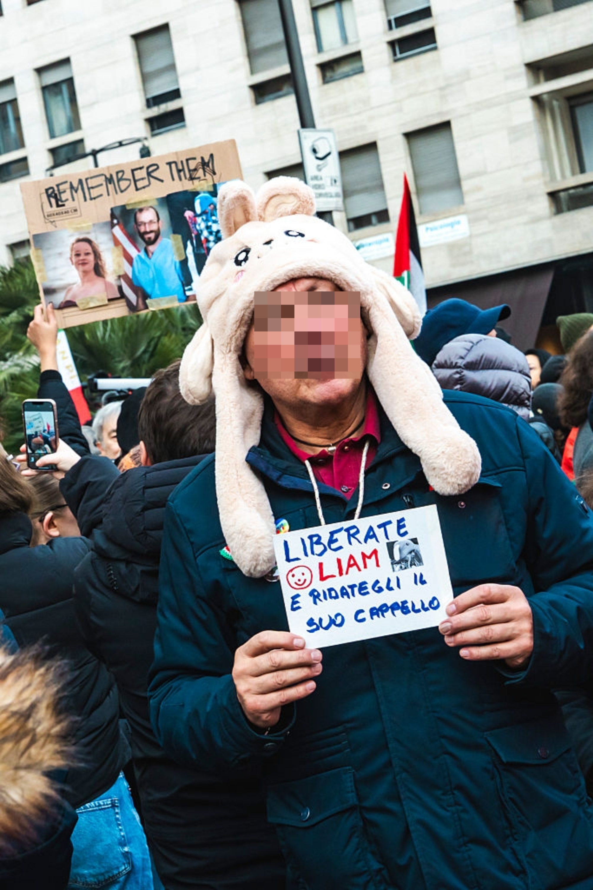 Person i en humoristisk kaninhatt holder skilt med italiensk tekst ved en protest, omgitt av andre med skilt