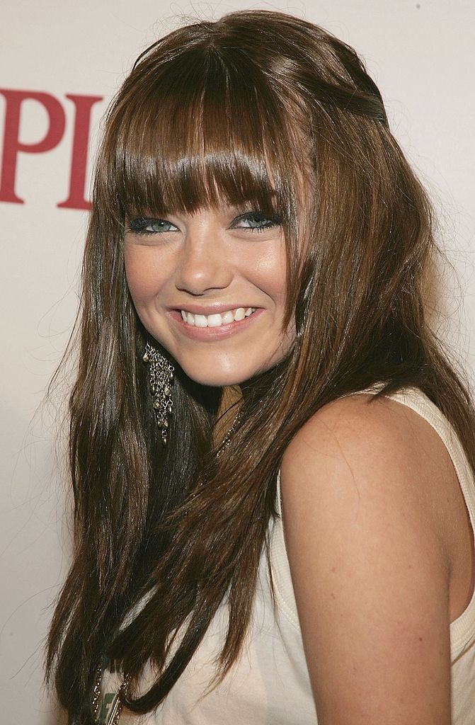 Person with agelong  hairsbreadth  and bangs smiling astatine  an event, wearing a sleeveless apical  and dangling earrings