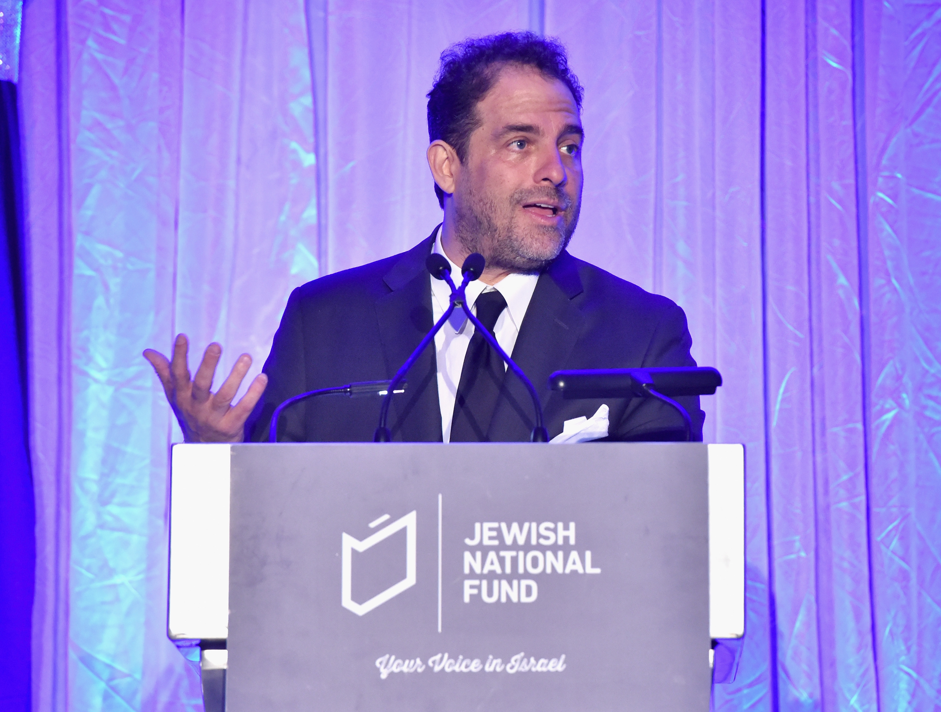 Brett Ratner i dress taler ved et podium med 