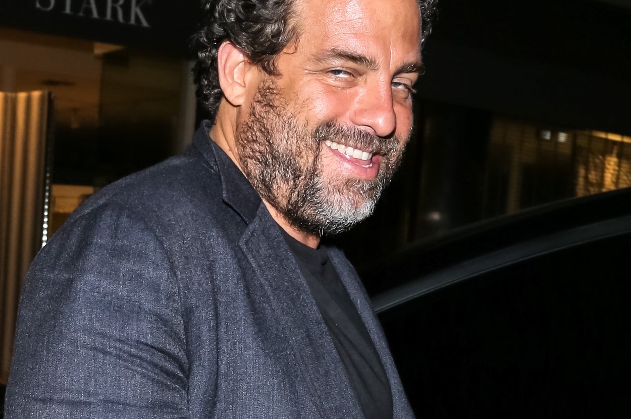 Person smiling, wearing a dark blazer over a t-shirt, standing outside a building