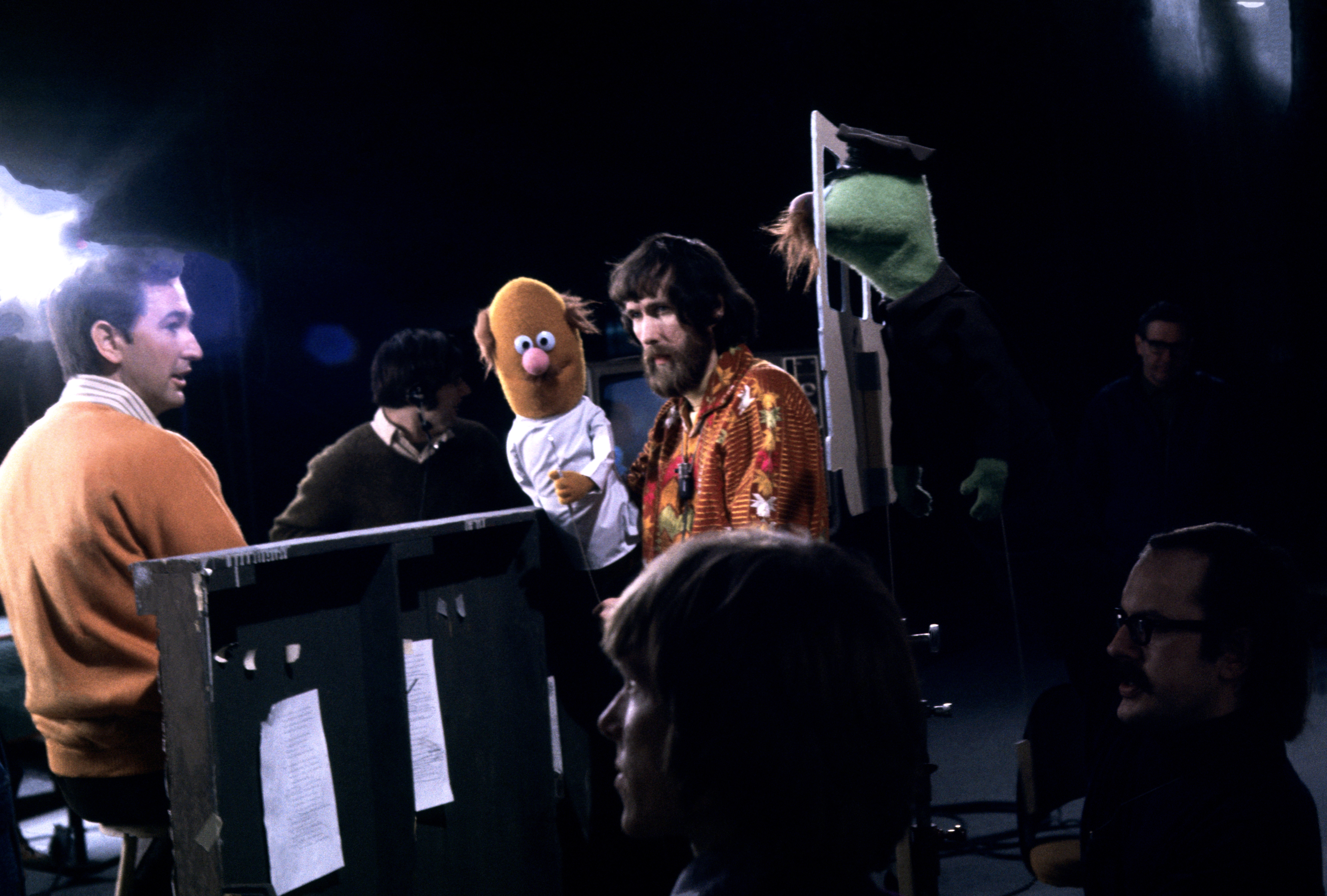 Puppeteers run Muppet characters down the scenes connected a set, including a greenish Muppet. Stage unit is preparing for a performance