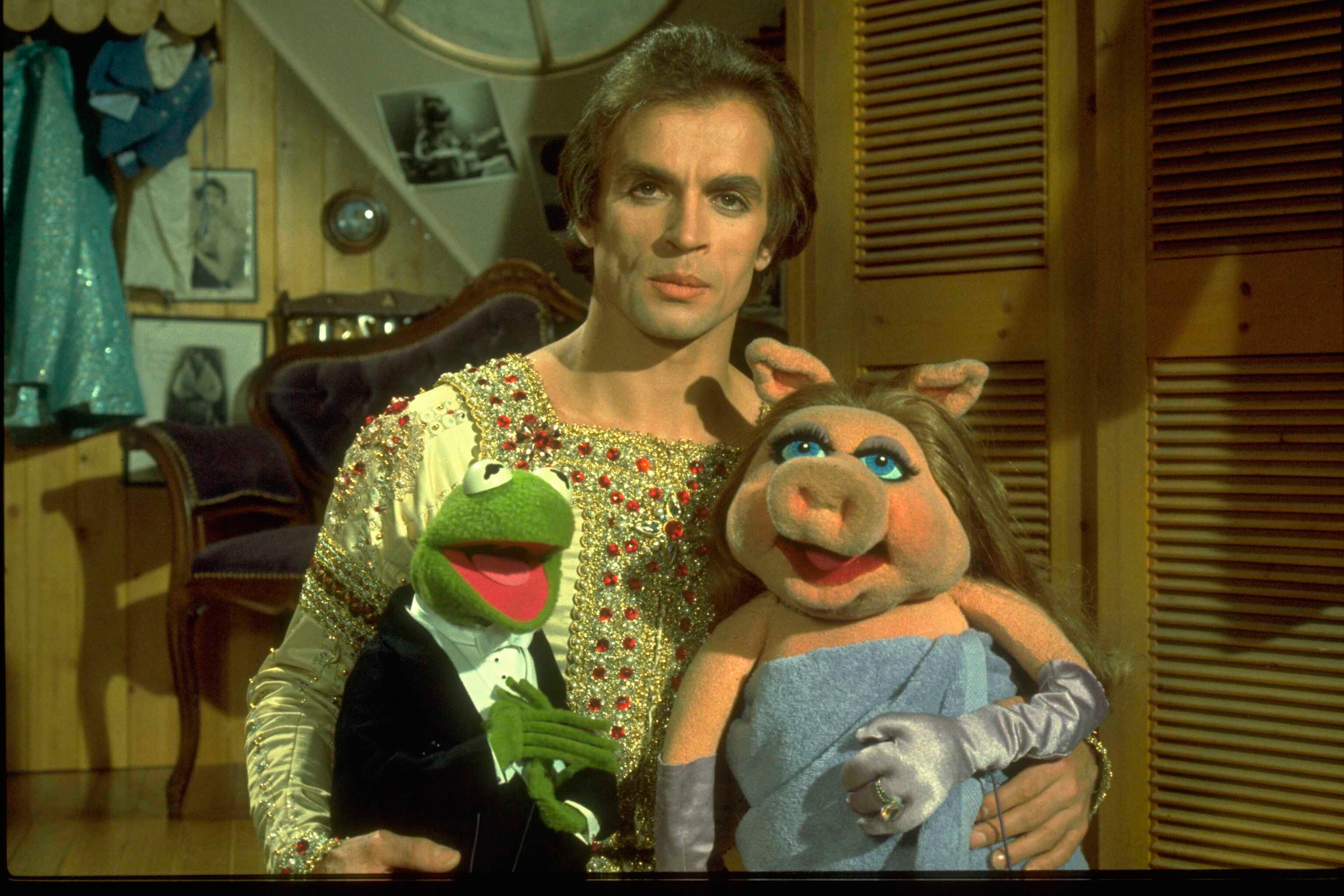Rudolf Nureyev successful a sequined outfit poses with Miss Piggy and Kermit the Frog puppets successful a country decorated with portraits