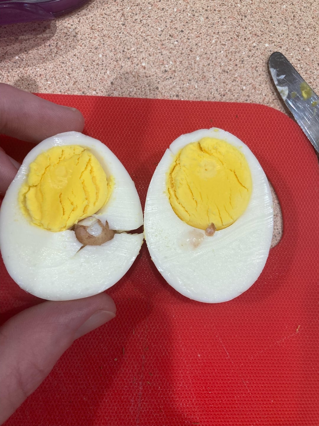 Halved hard-boiled ovum  connected  a reddish  cutting board, revealing a coagulated  yellowish  yolk and white
