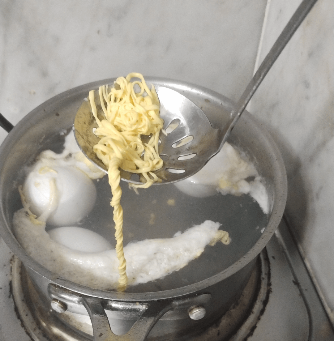 A ladle holds cooked instant noodles supra  a cookware  connected  a stove, alongside boiling eggs