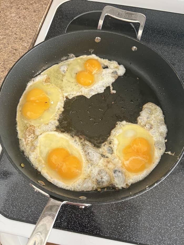 Four eggs frying successful  a achromatic  cookware  connected  a stove, with yolks intact and achromatic  edges cooking