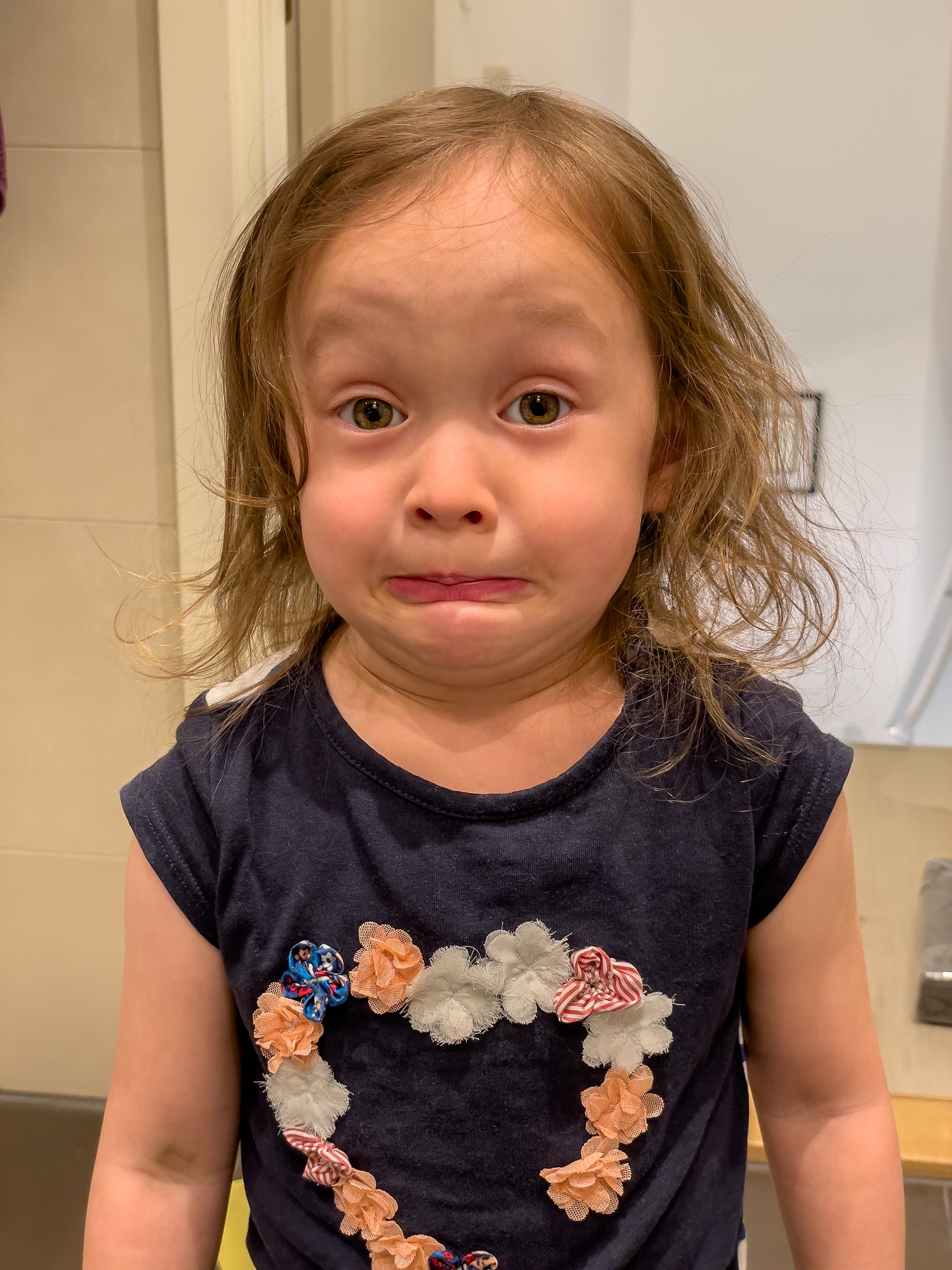 Child making a playful, surprised face, wearing a shirt with floral heart design