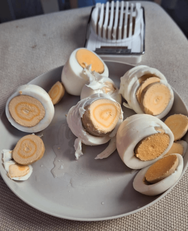Plate of peeled hard-boiled eggs with antithetic   spiral patterns inside, adjacent  to an ovum  slicer