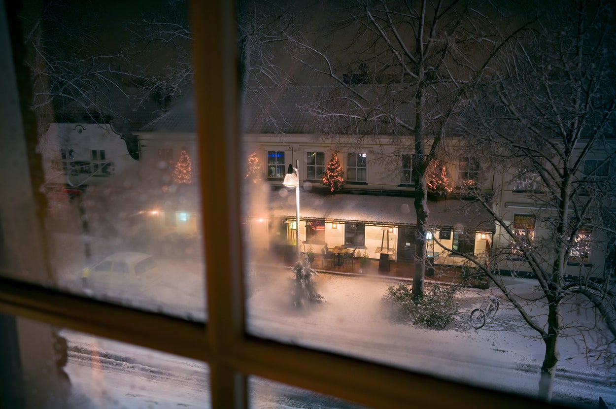 雪が積もった冬の夜、窓から見えるカフェと通りの様子。外にはクリスマス装飾も見える。