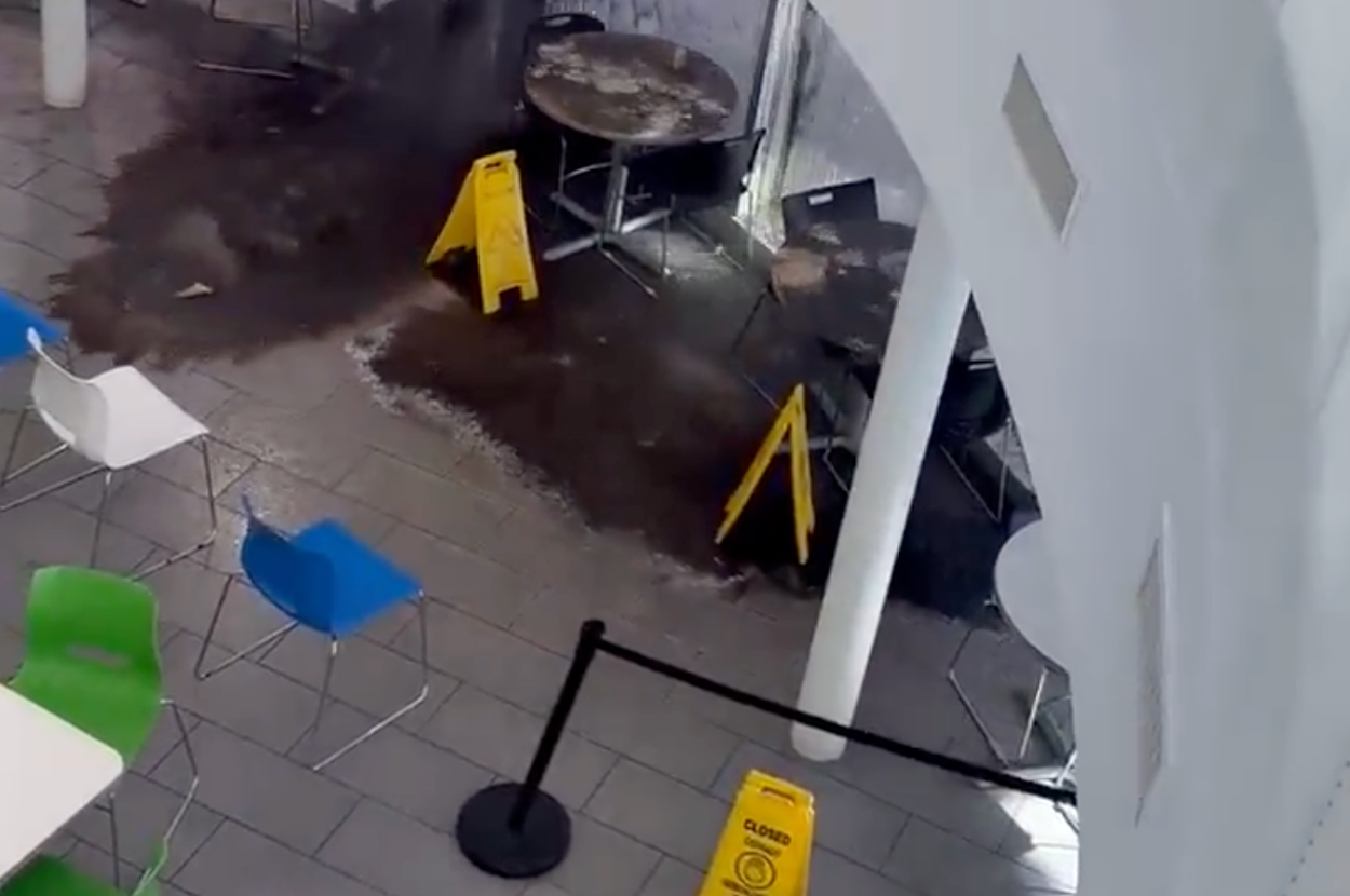 「注意」標識が立つカフェテリアで、床が水浸しになっている様子。