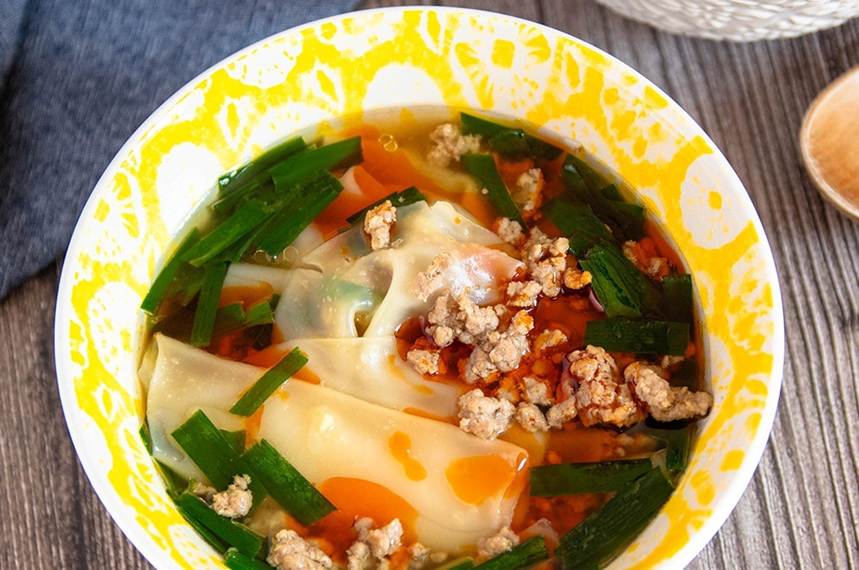 スープの中にギョーザの皮、ひき肉、ニラが入っている。木製のスプーンが横に置かれている。