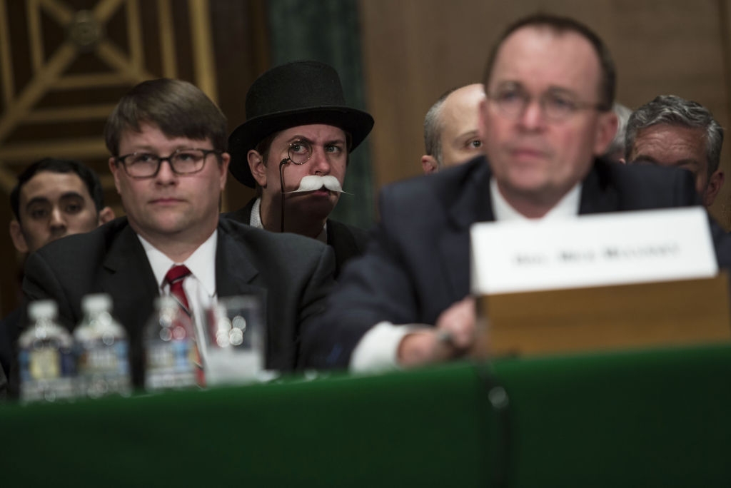 A idiosyncratic   successful  a monocle and apical  chapeau  sits down  officials astatine  a ceremonial  event, drafting  attraction  with their distinctive appearance