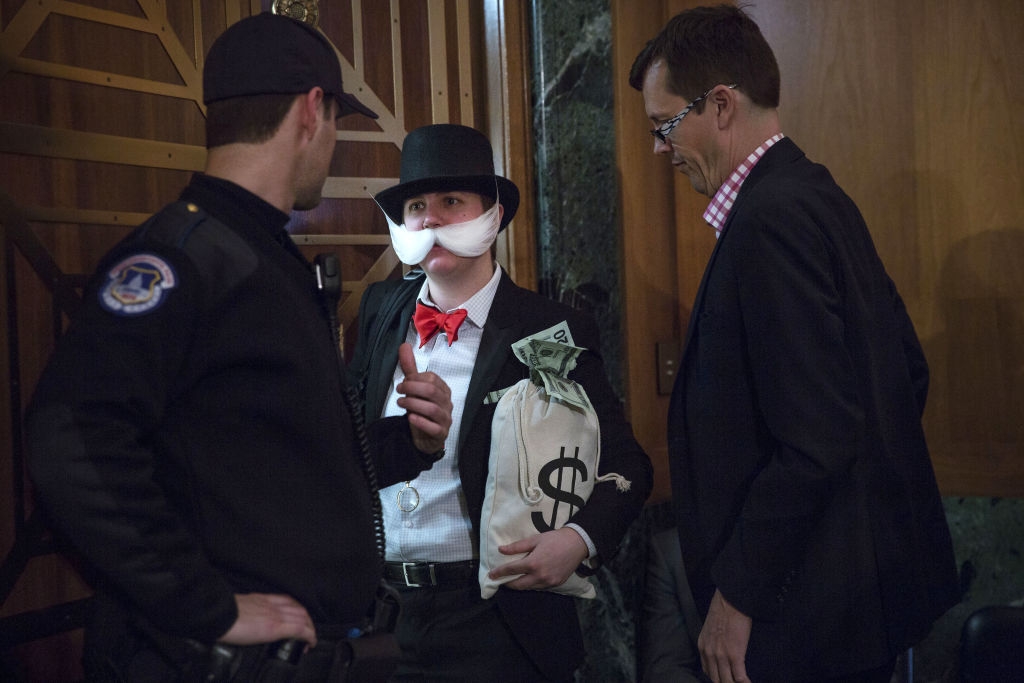 Person dressed arsenic  a banker with a mustache, apical  hat, and wealth  bag, speaking to a information    defender  and different  idiosyncratic   successful  a suit