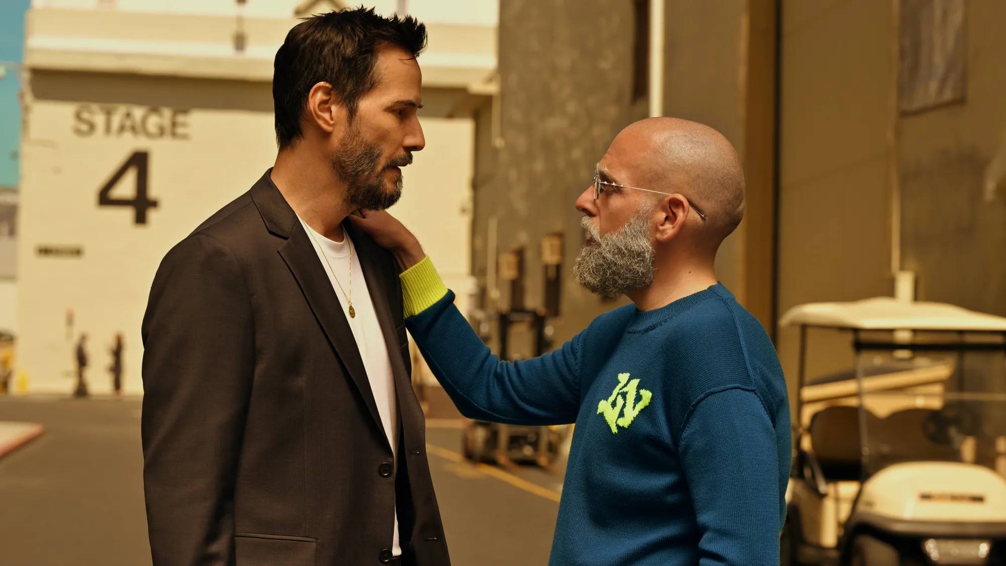 Two men converse outdoors adjacent   a workplace  stage. One wears a casual suit, the different   a sweater with agleam  cuffs and a logo