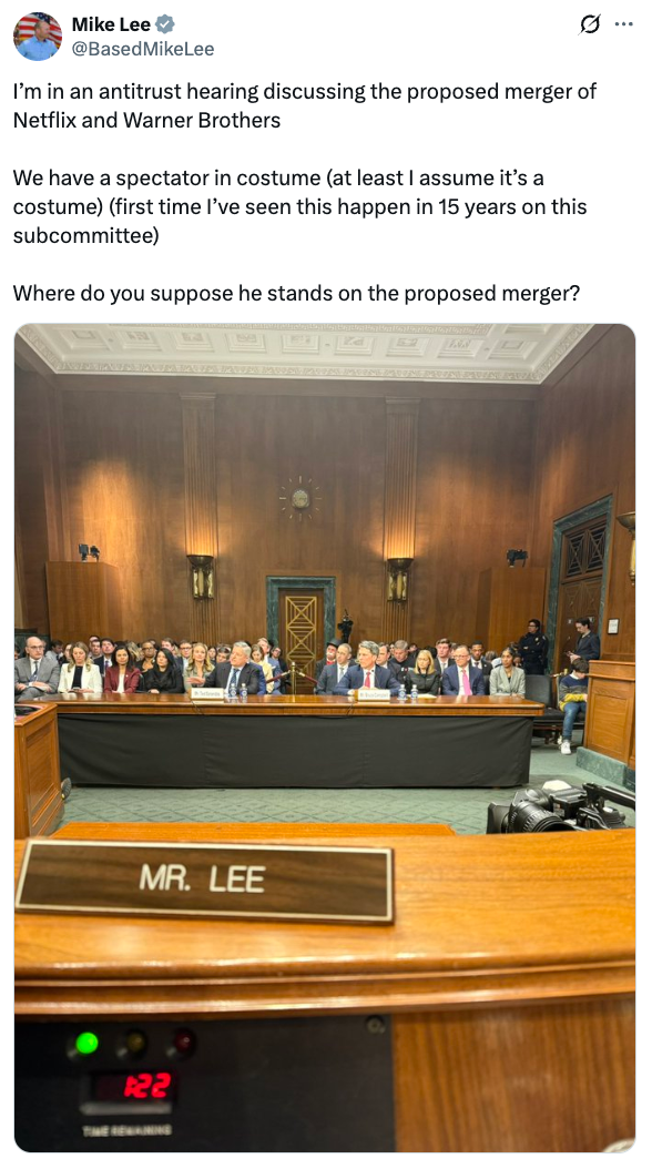 Courtroom with panelists astatine  an antitrust proceeding  connected  a projected  Netflix and Warner Brothers merger; a idiosyncratic   successful  costume is present