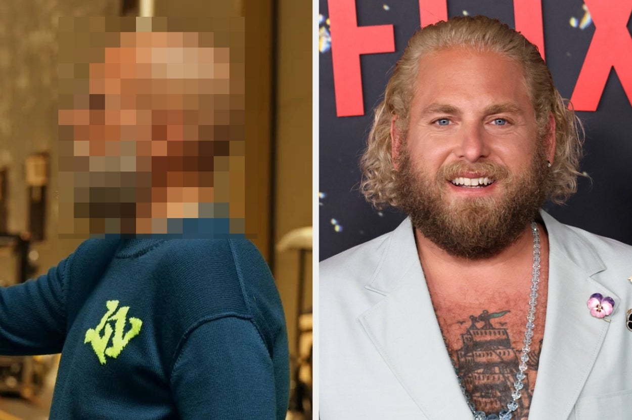 Person on the right, with curly hair and a beard, wearing a light suit with a chain necklace, smiles at a celebrity event