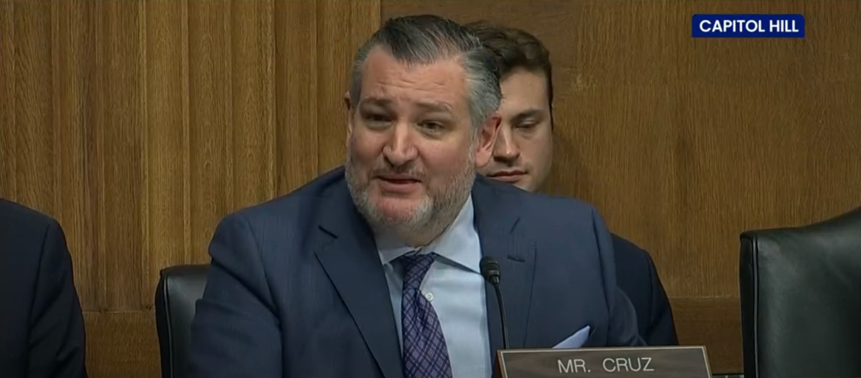 A antheral   successful  a suit   and necktie  speaks astatine  a Capitol Hill hearing, seated successful  beforehand   of a woody  sheet  with a "Mr. Cruz" nameplate
