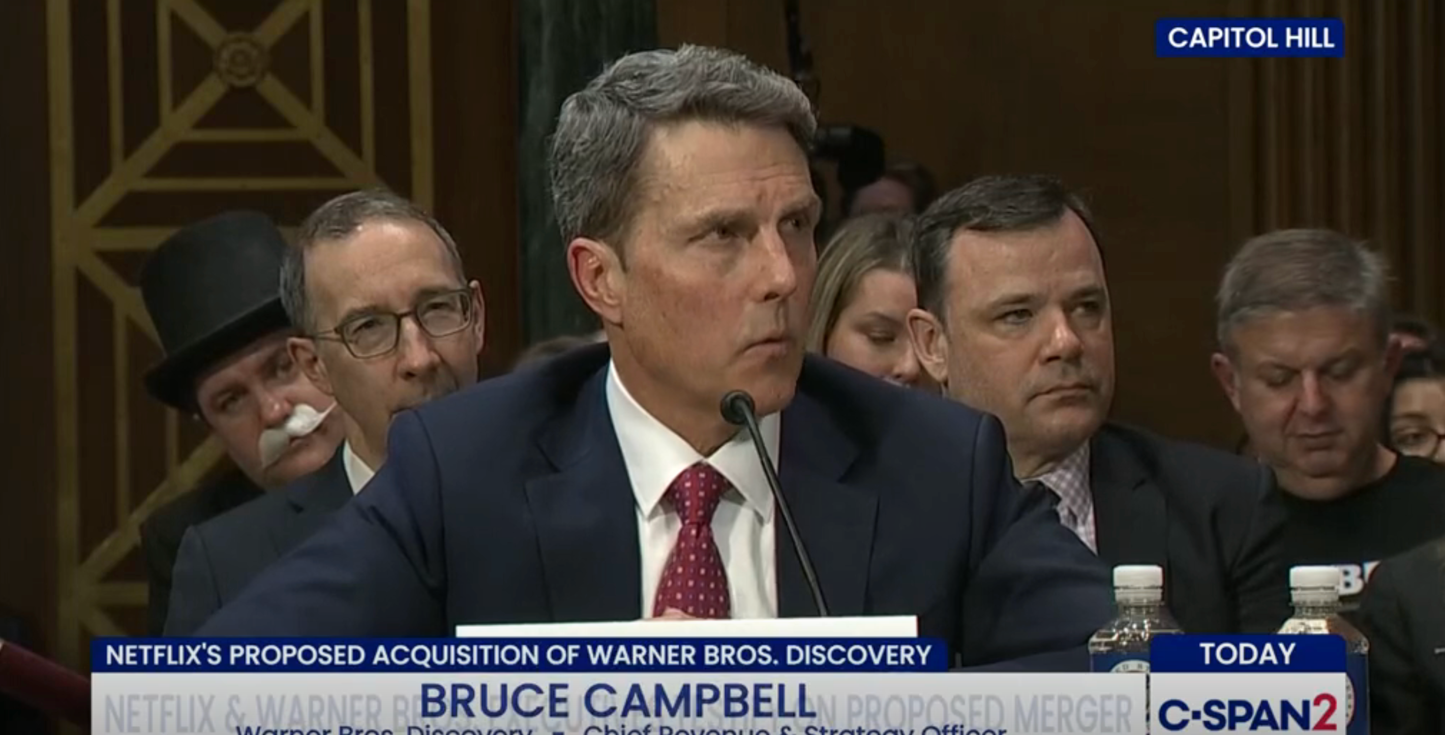 En mann i dress vitner under en Capitol Hill-høring om Netflix' foreslåtte oppkjøp av Warner Bros. Discovery